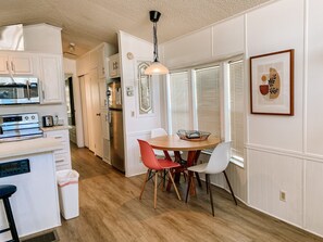 A modern kitchen with white cabinetry, stainless steel appliances, and a dining area with a wooden table and chairs. - Albey at the Beach (Sarasota)