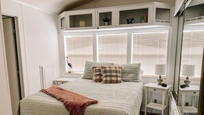 A neatly arranged bedroom with a bed, bedside tables, a mirror, and built-in shelving with decorative items. - Albey at the Beach (Sarasota)