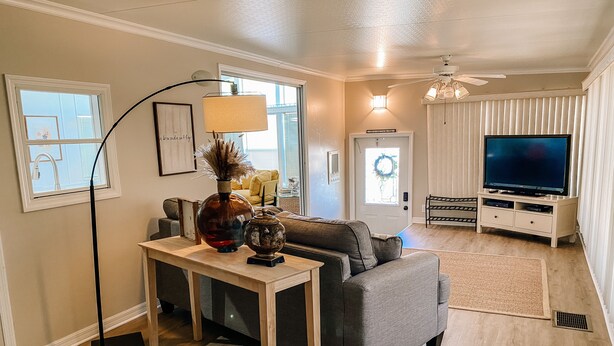 A living room with a grey sofa, a coffee table, a TV stand with a flat-screen TV, a floor lamp, and a door with a wreath. - Albey at the Beach (Sarasota)