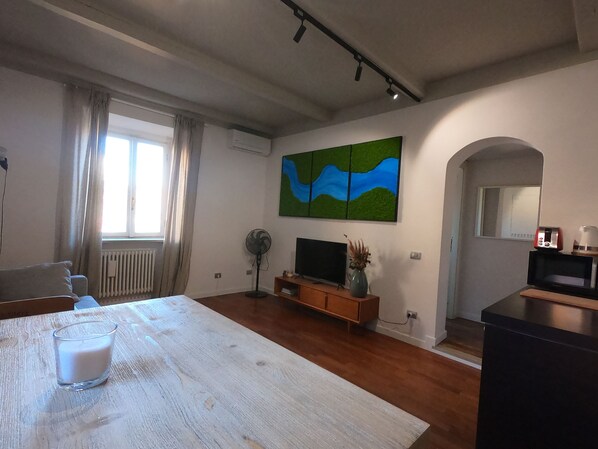 Una sala de estar moderna con una mesa de comedor de madera, un televisor de pantalla plana, una cafetera y un cuadro en la pared.