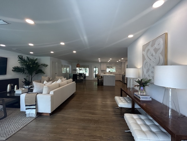 A spacious living room with a large sofa, a dining area, and a kitchen in the background.