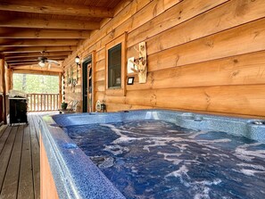 A wooden cabin with a hot tub on the porch.