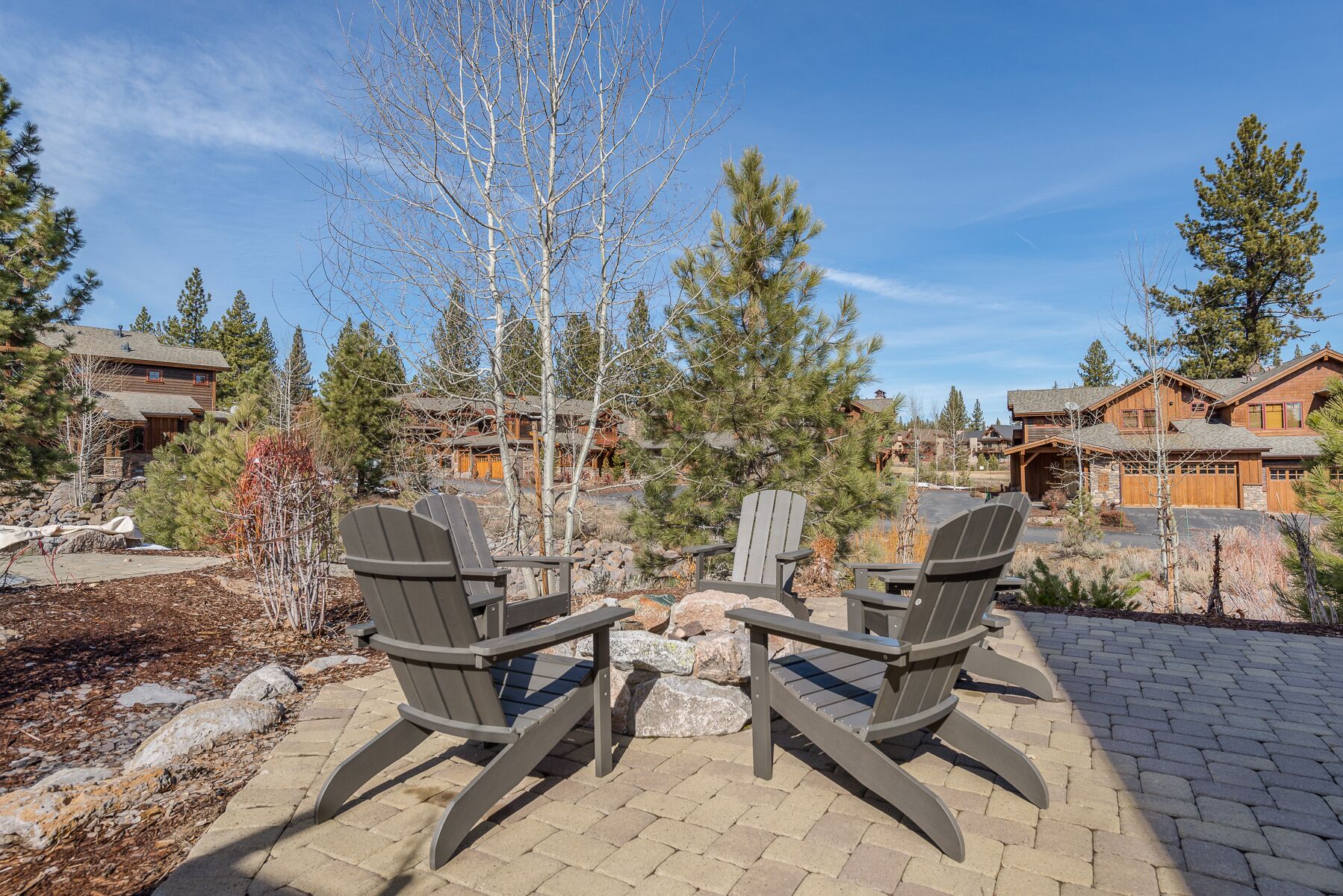 Een terras met Adirondack-stoelen, een stenen tafel en uitzicht op gebouwen in lodge-stijl, omringd door bomen.
