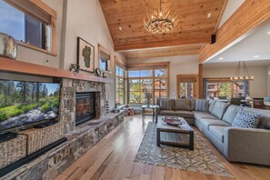 Cozy living area with a fireplace, sofa, and large TV, offering a view of the surrounding landscape.