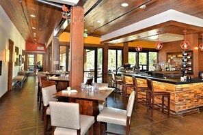 Enjoy meals in our spacious dining area with wooden tables and chairs, a bar with a stone counter, and large windows offering views of the outdoors.