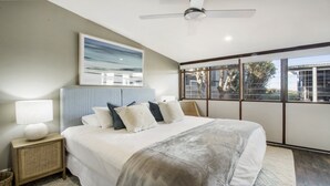 A modern bedroom with a large bed, a ceiling fan, a city view through large windows, and a framed artwork above the bed. - Luxury absolute beachfront home (Noraville)