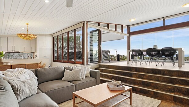 A modern living room with a grey sofa, a wooden coffee table, and a view of outdoor seating and stairs. - Luxury absolute beachfront home (Noraville)