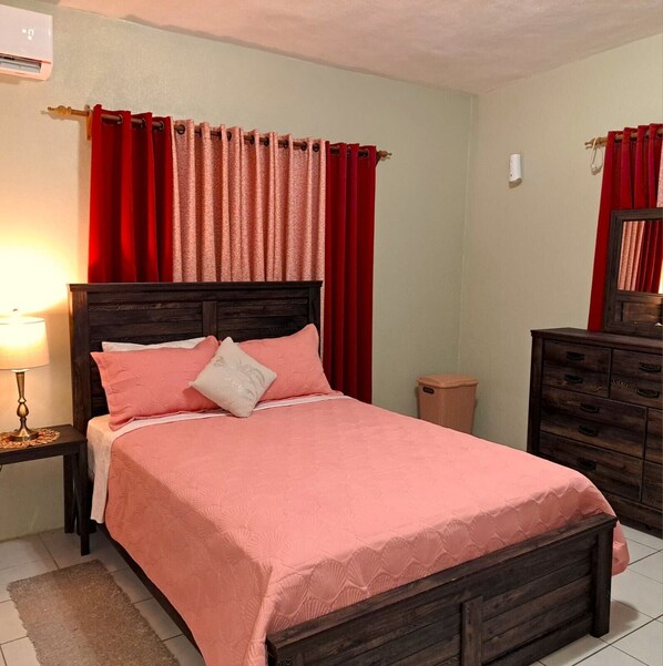 Een slaapkamer met een bed, nachtkastje, dressoir en prullenbak.