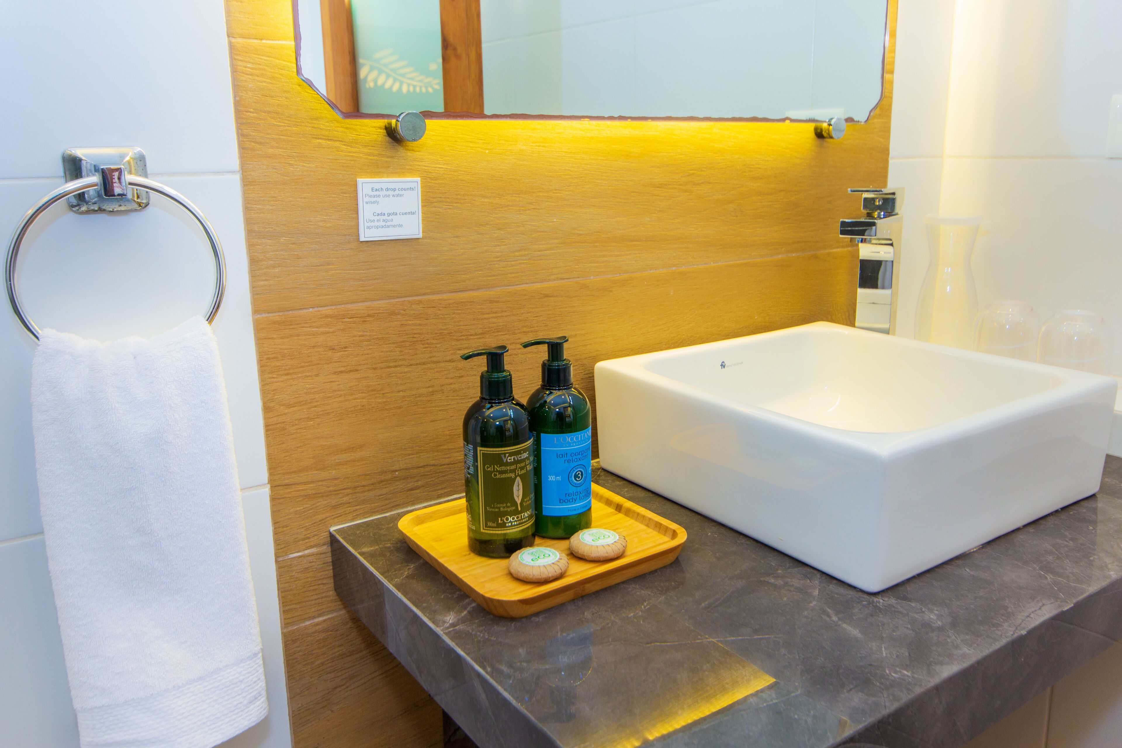 A bathroom with a wooden vanity, a white sink, and two bottles of lotion on a tray.