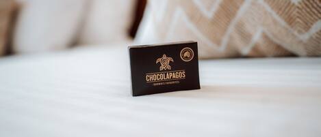 Tarjeta de presentación negra con texto dorado y un logotipo sobre un cubrecolchón blanco.
