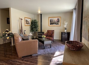Een woonkamer met een bank, fauteuil, salontafel en een open haard. Twee ingekaderde foto's hangen aan de muur en er staat een plant op een bijzettafeltje.