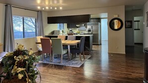A modern kitchen with dark cabinets, a refrigerator, and a dining area with a table and chairs. - Grand Canyon Williams Deluxe Vacation Getaway AC (Williams)
