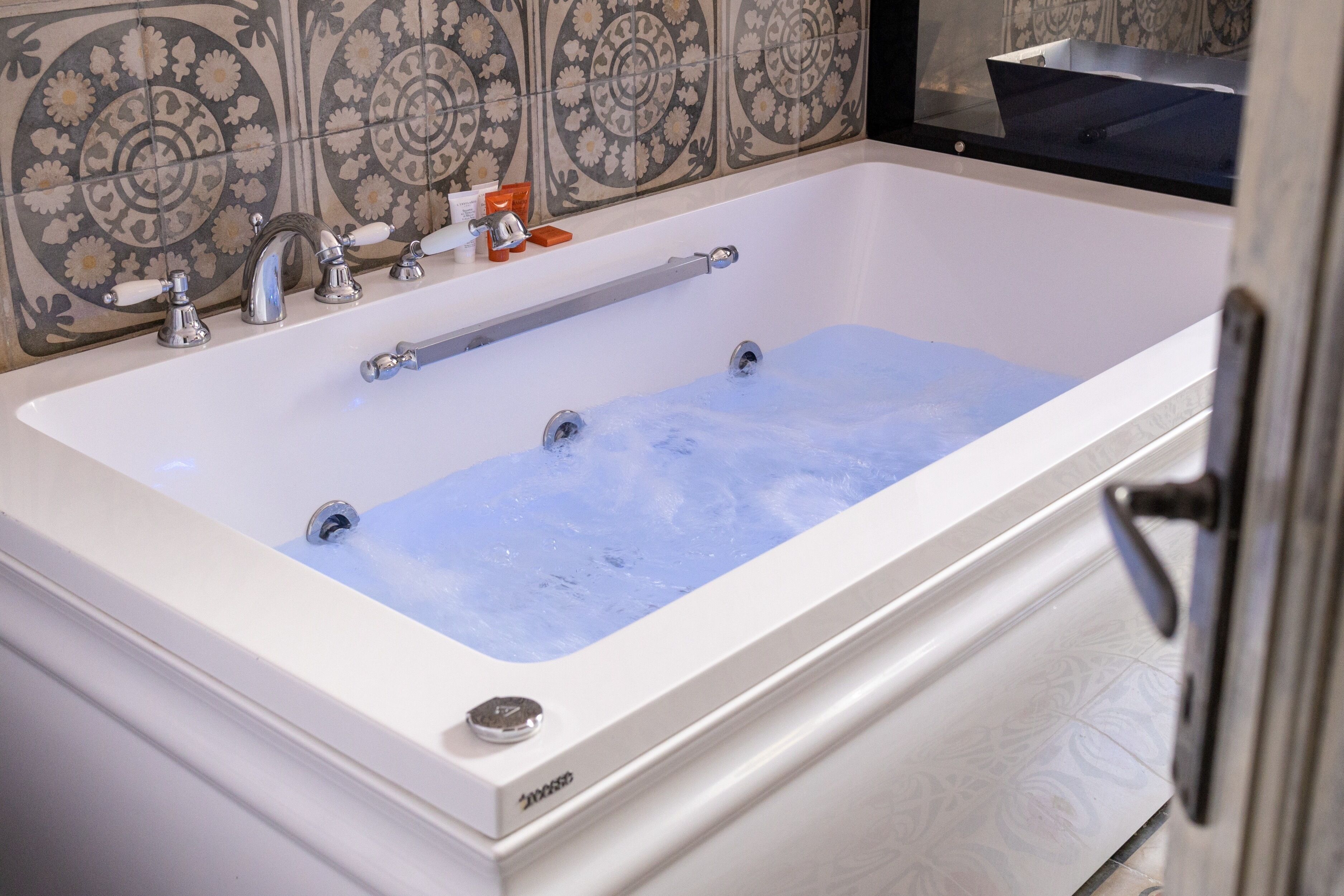 A modern bathroom with a white bathtub, chrome fixtures, and a decorative tile backsplash.