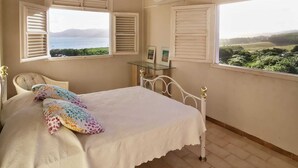 Un dormitorio con cama, una silla y dos ventanas con contraventanas.