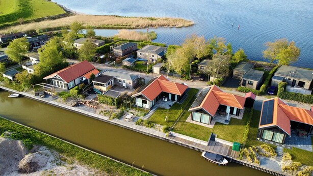 A residential area with houses along a canal, featuring modern architecture and a dock with a boat. - Vacation home with access to the water (Anjum)
