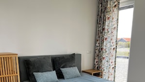 Un lit avec une tête de lit rembourrée de couleur grise, une table de chevet en bois et un rideau à motifs floraux.