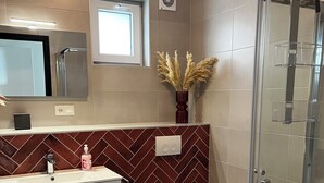 Une salle de bain moderne avec un mur orné d’un motif en chevrons, une douche en verre et un meuble-lavabo agrémenté d’un miroir et d’un vase rempli de plumes d’herbe des pampas.