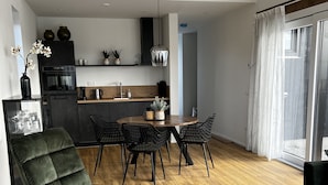 A modern kitchen with dark cabinetry, a central island, and a dining area with a round table and chairs. - Vacation home with access to the water (Anjum)