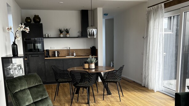 Une cuisine moderne avec des meubles de couleur sombre, un îlot central et un coin repas comprenant une table ronde et des chaises.