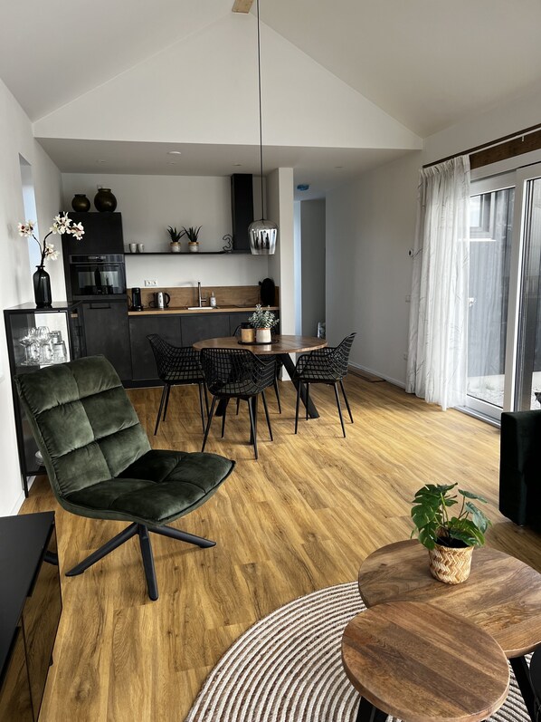 A modern kitchen with dark cabinetry, a central island, and a dining area with a round table and chairs. - Vacation home with access to the water (Anjum)
