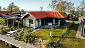 Une maison moderne avec un toit rouge, de grandes fenêtres et une pelouse bien entretenue.