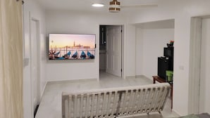 A bedroom with a bed, a ceiling fan, a TV mounted on the wall, and a door leading to another room. - Slice of Paradise- 2 mins from Spotts Beach! (Patricks Island)