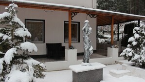 Un área al aire libre cubierta de nieve con una estatua, un porche cubierto y árboles cargados de nieve.