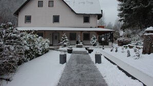 Una casa de dos pisos con techo nevado y un camino que lleva a la entrada.