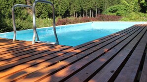 Una terraza de madera con escaleras metálicas junto a la piscina y agua cristalina, rodeada de abundante vegetación.