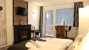 Habitación de hotel con chimenea, cama con ropa de cama blanca, escritorio con una silla y vista por la ventana.