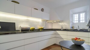 Una cocina moderna con armarios blancos, una encimera negra y una mesa redonda con un frutero.