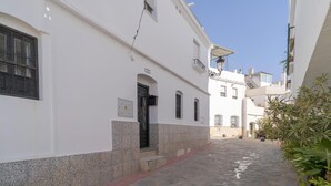 Una calle estrecha con edificios blancos, un camino empedrado y una pequeña planta a la derecha.
