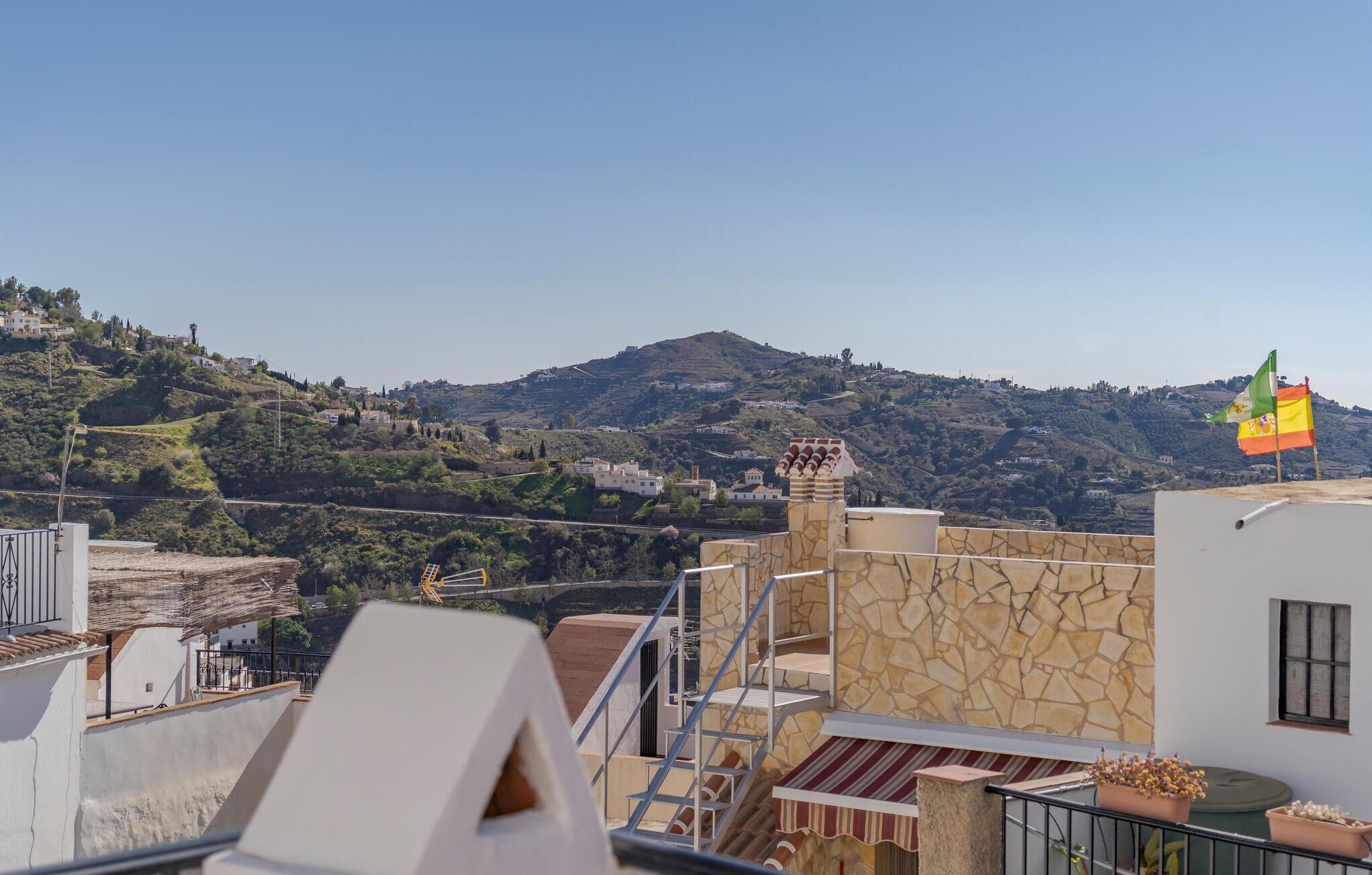 A rooftop terrace with a stone wall, a flag, and a view of a hilly landscape.