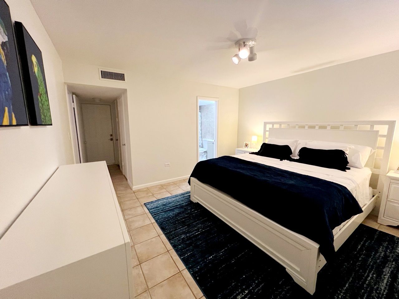 A bedroom with a bed, bedside tables, a ceiling fan, and a door leading to another room.