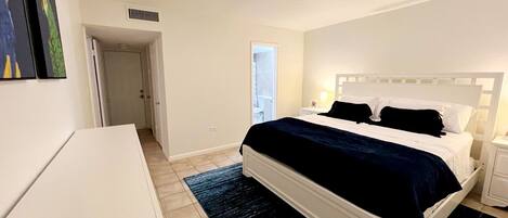 A bedroom with a bed, bedside tables, a ceiling fan, and a door leading to another room.