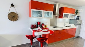 Una cocina moderna con armarios rojos, una encimera blanca y dos taburetes rojos.