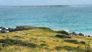Un paisaje costero con un primer plano herboso, afloramientos rocosos y vistas al mar y a tierra distante.