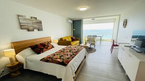 Habitación de hotel con cama, sofá, televisión y vista al mar.