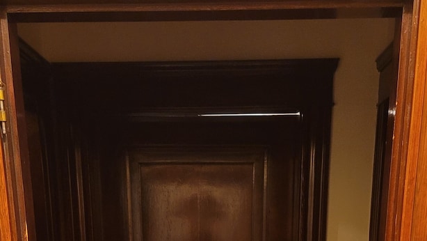 Une porte en bois avec une poignée de porte en laiton, un paillasson vert et une prise de courant sur le mur, à droite.