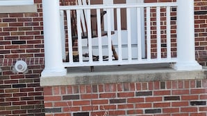 Une maison en briques avec une porte d’entrée blanche, un petit porche doté d’une balustrade blanche et une fenêtre sur le côté gauche.