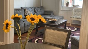 Un salón con un sofá gris, una mesa de centro con un cuenco, y una silla. Girasoles en un jarrón sobre la mesa.