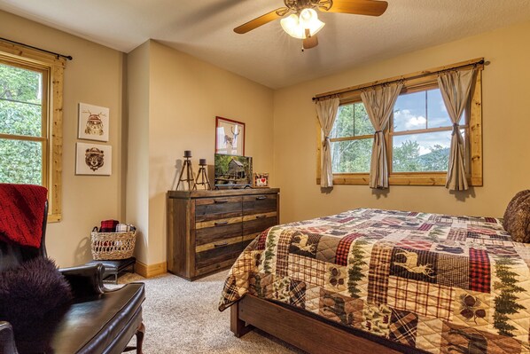 Quarto com uma cama grande, cómoda de madeira, cadeira e ventoinha no teto.