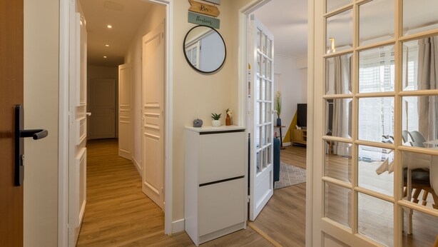 A hallway with a wooden floor, white doors, a small white cabinet with decorative items, and a mirror on the wall. - Spacious, cosy and chic apartment (Laval)