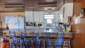 Een keuken met een centraal eiland, houten stoelen en witte kasten.