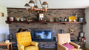 Een gezellige woonkamer met een met baksteen beklede open haard, twee fauteuils, een houten salontafel en een televisie.