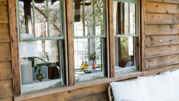 Une cabane en bois avec de grandes fenêtres, un fauteuil en osier et un canapé blanc.