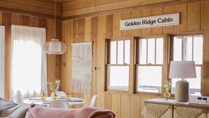 L’intérieur d’un chalet avec un plafond en bois, un canapé avec des coussins, une table ornée d’une décoration murale en macramé et une enseigne indiquant « Golden Ridge Cabin ».