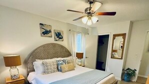Een slaapkamer met een bed, nachtkastje, plafondventilator en een deur.