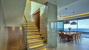 A modern interior with a staircase, a dining area, and large windows offering a view of the ocean. - Sparkling ocean views with heated pool (Rodhia)