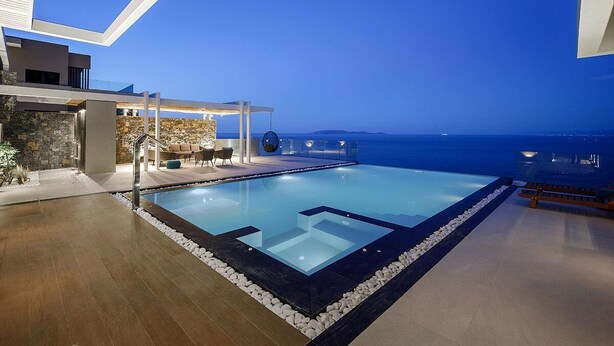 Ein moderner Infinity-Pool mit freiem Blick auf den Ozean, einer überdachten Sitzgruppe und einer Steinmauer.